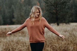 Eine Frau im Orange-Pinken Pullover, Lächelnd, auf einem Feld.